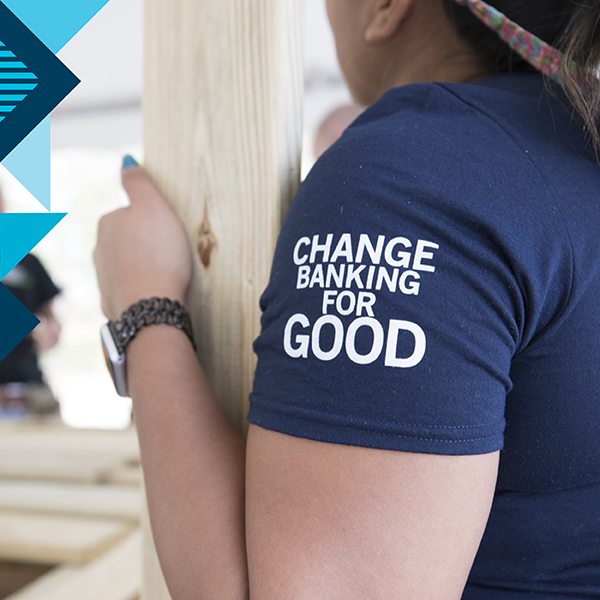 Capital One associate volunteering is carrying a 2x4, with the sleeve of her shirt saying "Change Banking for Good"